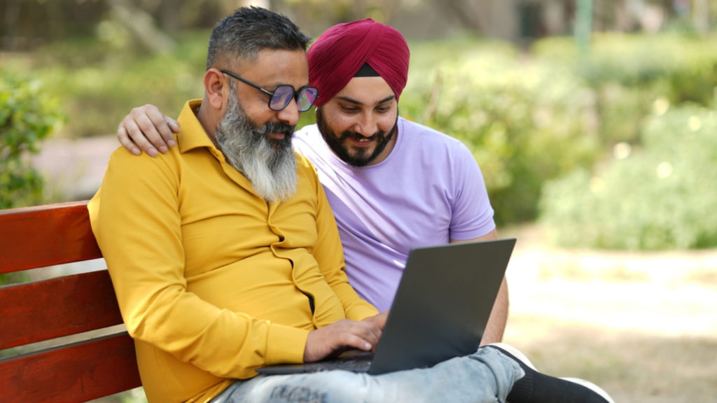 Two men sitting on a bench, engaged with a laptop, exploring options for their Canada Work Permit.